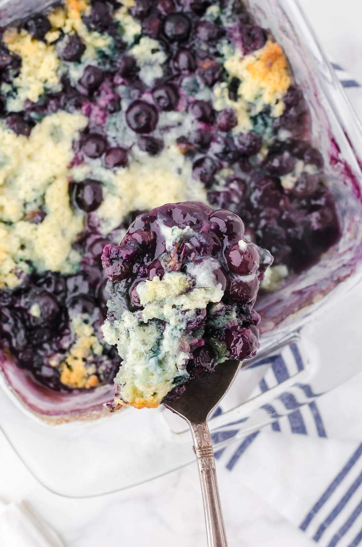 Juicy blueberry cobbler in baking dish with spoon scooping up a serving.