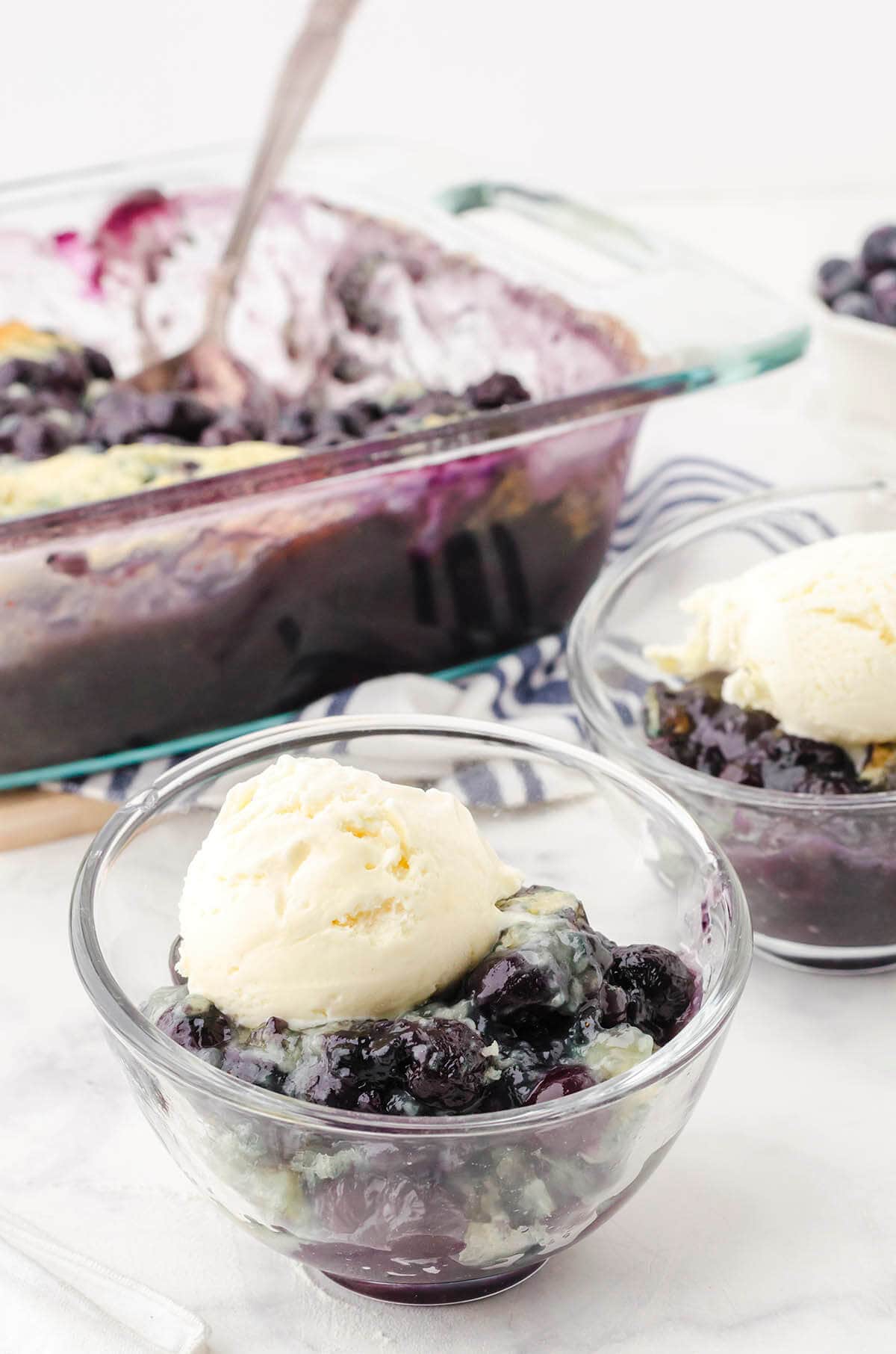 Blueberry cobbler from scratch in dish and served in bowls topped with vanilla ice cream. 