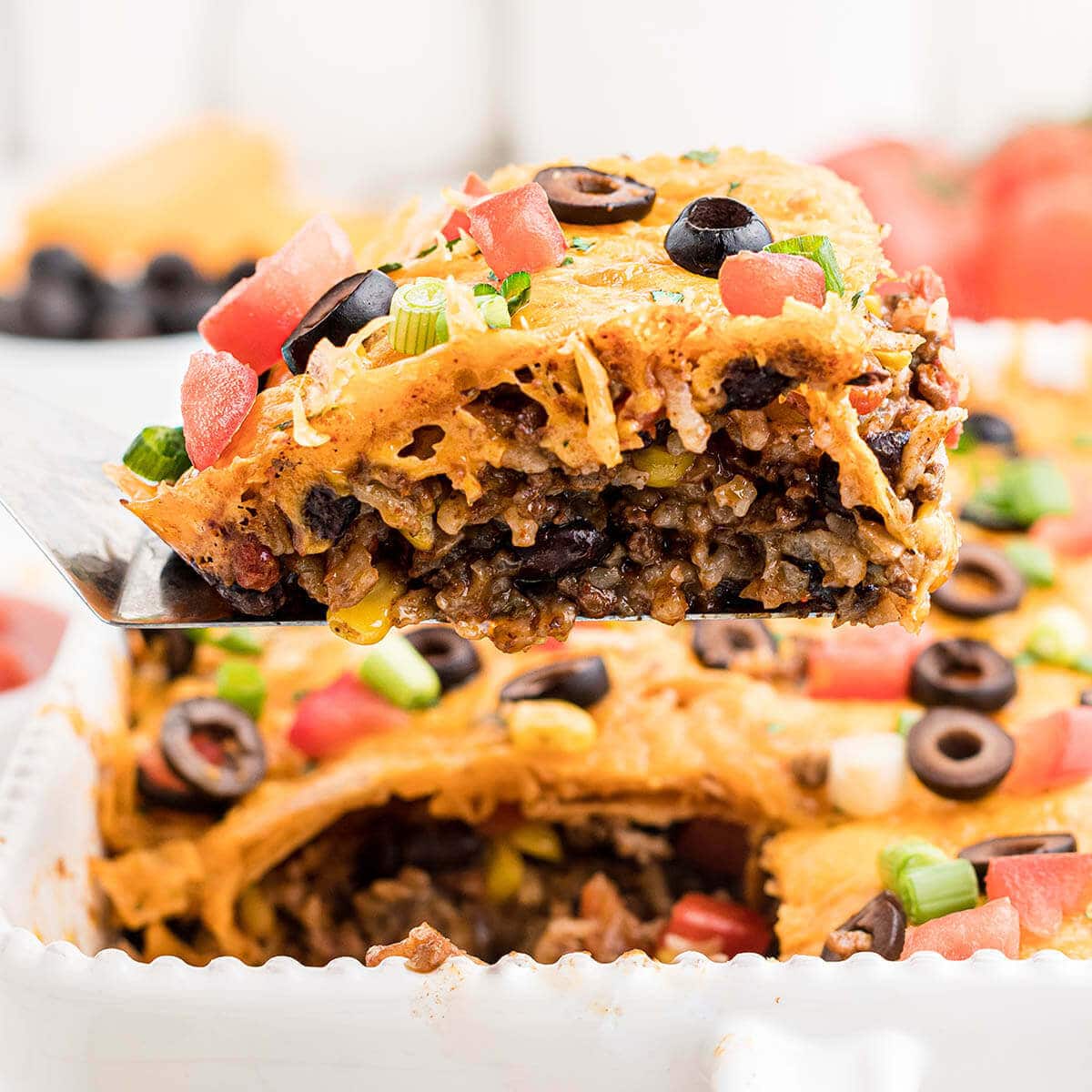 Ground beef cheesy taco casserole in baking dish with serving spoon. 