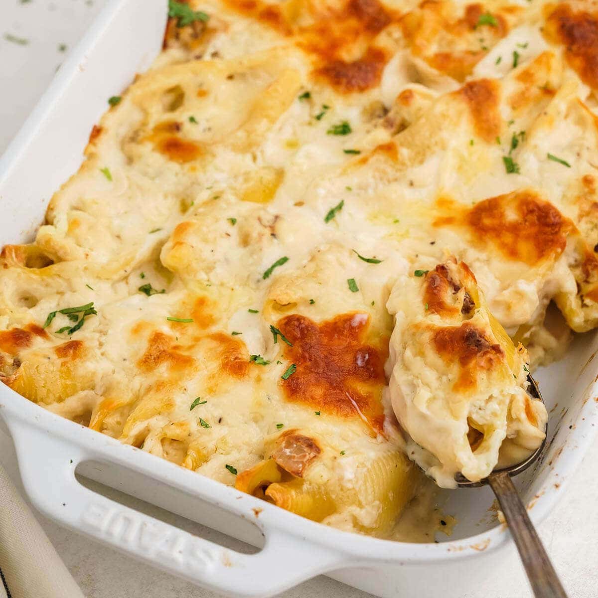 Chicken Alfredo Stuffed Shells in baking dish with serving spoon.