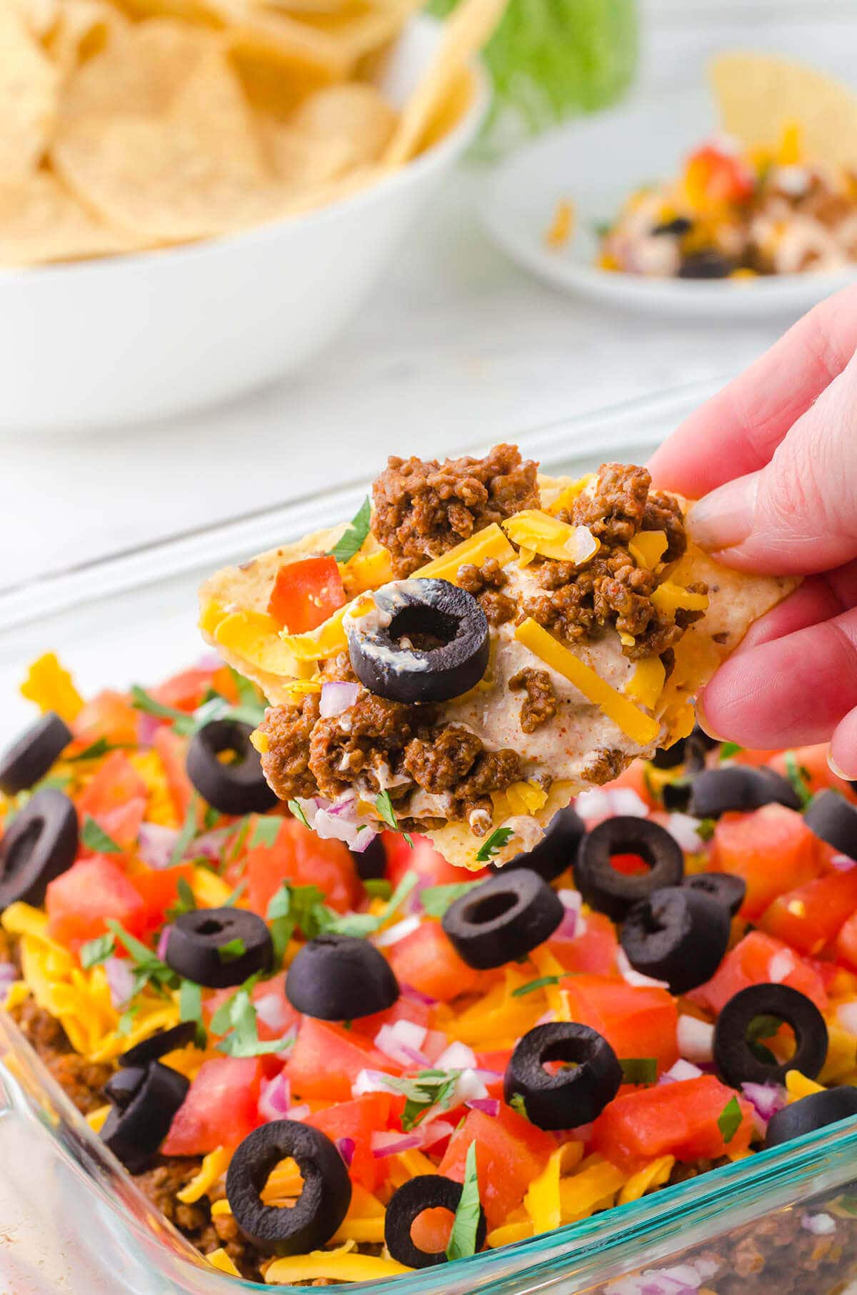 Ground beef taco dip in casserole dish with chip scooping it. 