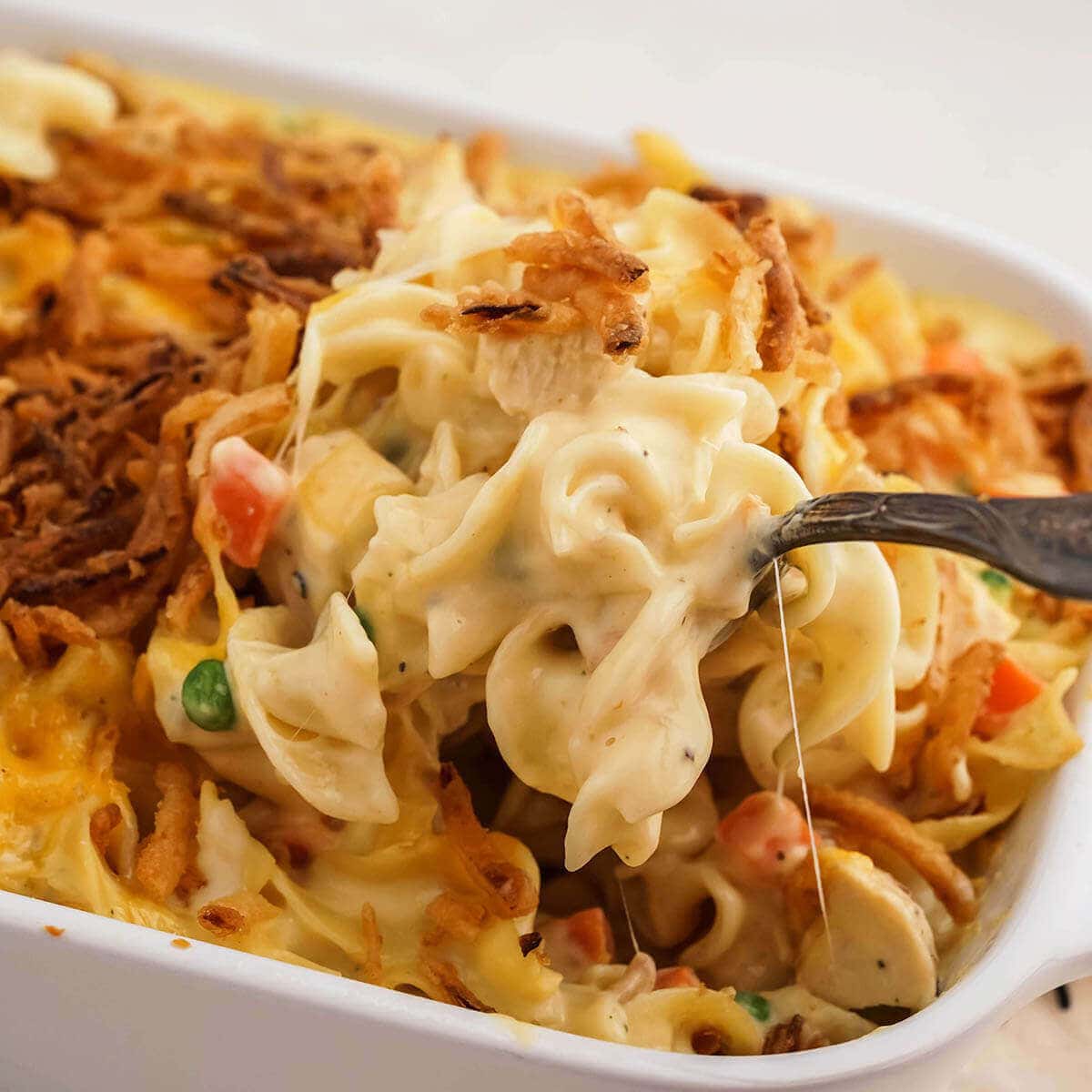 Cheesy chicken noodle casserole in baking dish with serving spoon.