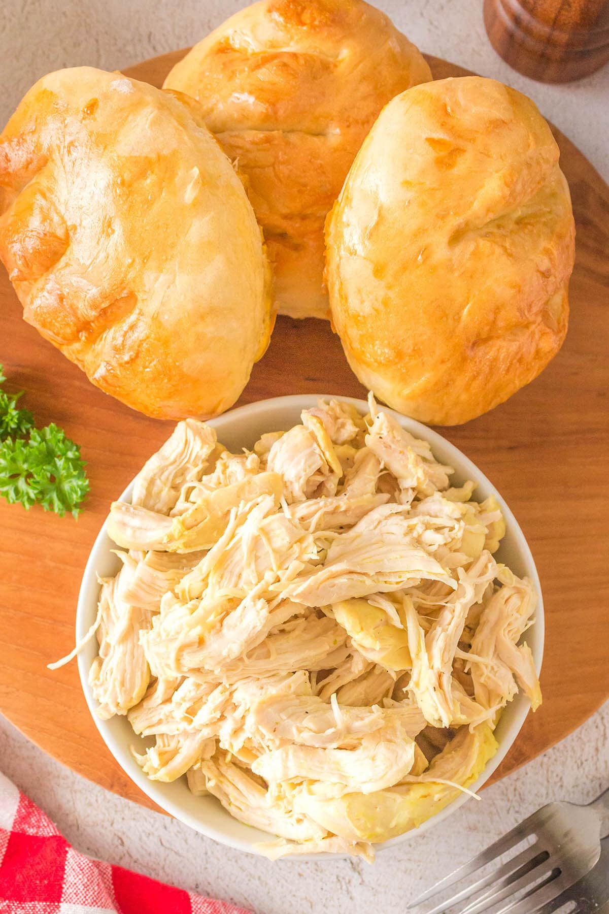 Lemon pepper shredded chicken in bowl with crusty rolls to make sandwiches with.