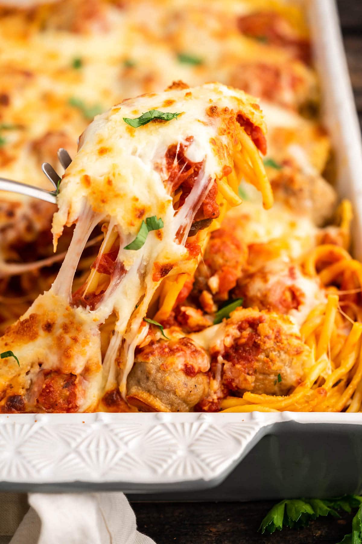Cheesy spaghetti and meatball casserole with spoon dishing out a helping.