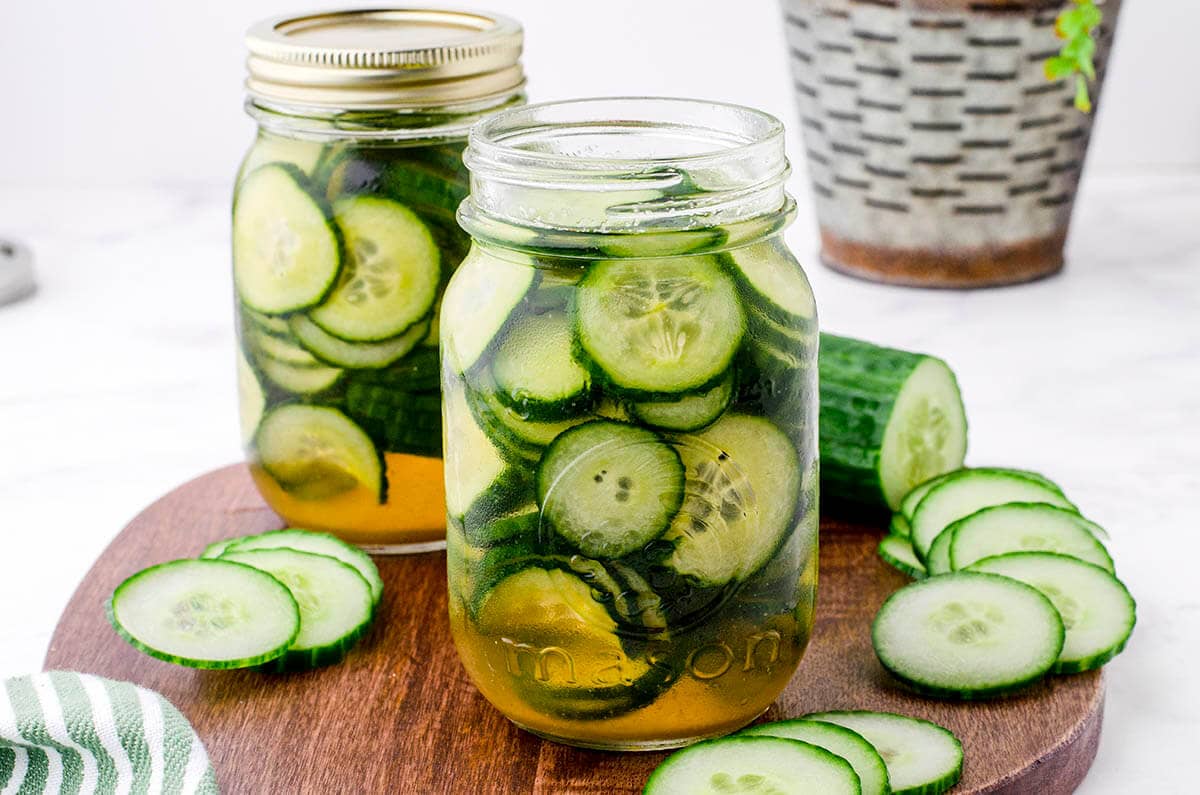 Sliced cucumbers surrounding a jar of pickles.