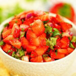 Strawberry salsa in white bowl surrounded by tortilla chips.