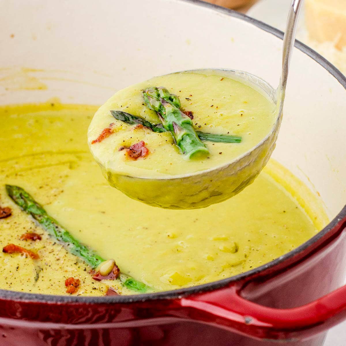 Stockpot filled with asparagus soup, with ladle scooping out a serving.