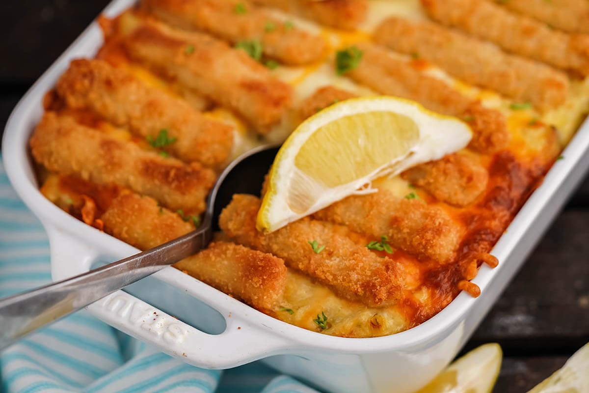 Cheesy fish stick casserole in baking dish with spoon.