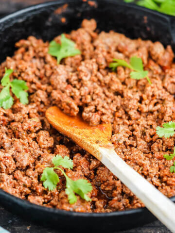 Browned taco meat in skillet with wooden spoon.