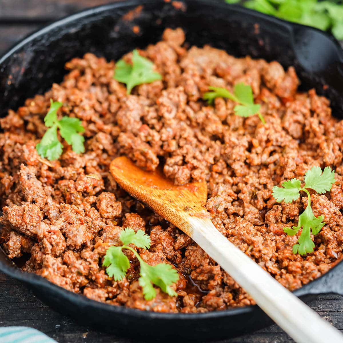 Browned taco meat in skillet with wooden spoon.