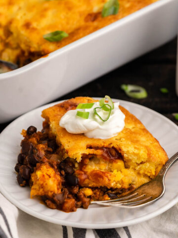 A serving of tamale pie on plate with fork, with casserole in the background.