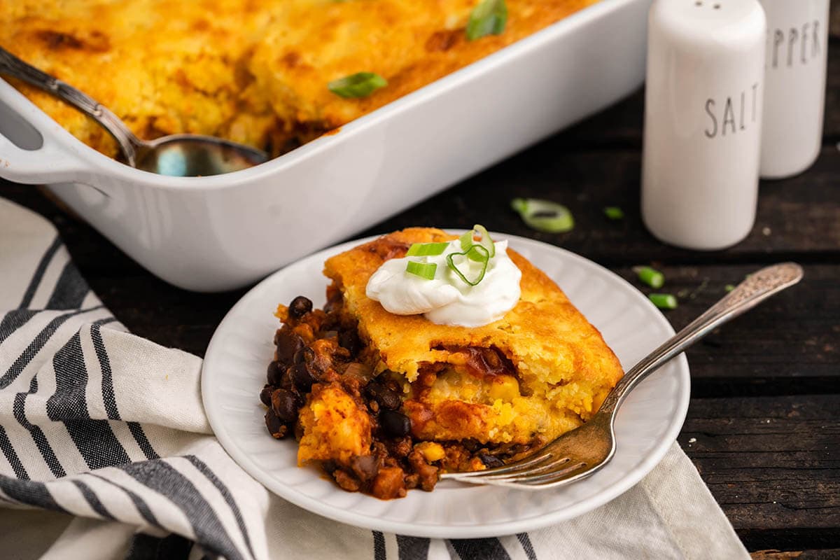 Serving of cornbread pie on plate with fork, with baking dish in the background.