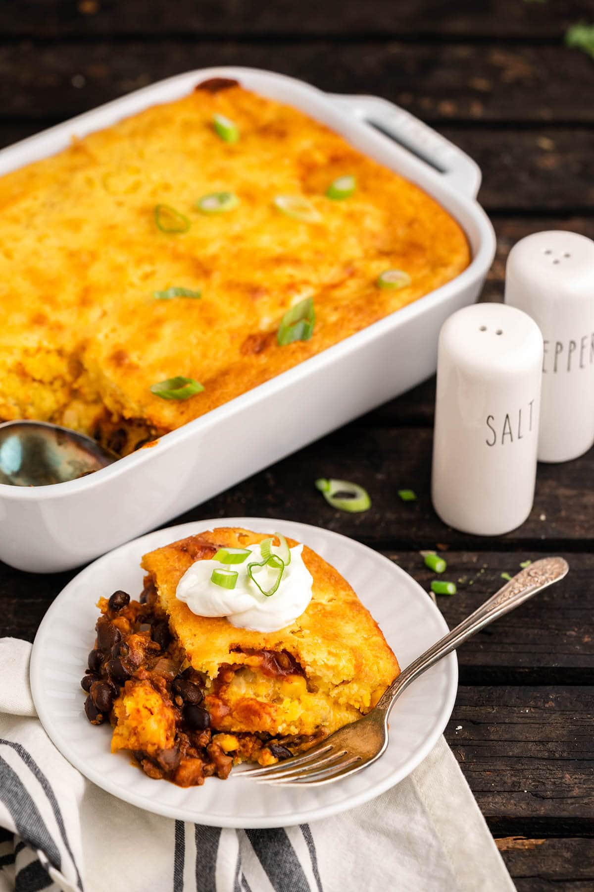 Cornbread casserole on plate with fork, with baked casserole in the background.