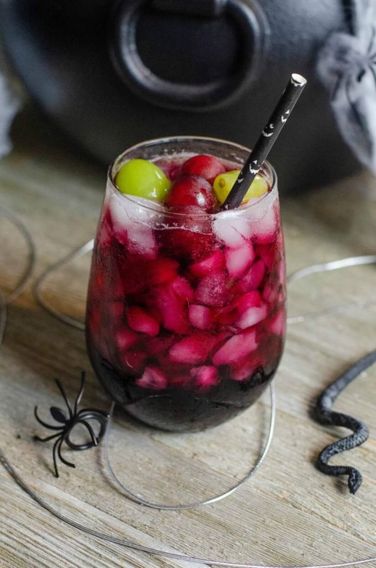 Purple drink topped with green and red grapes surround by halloween decor.