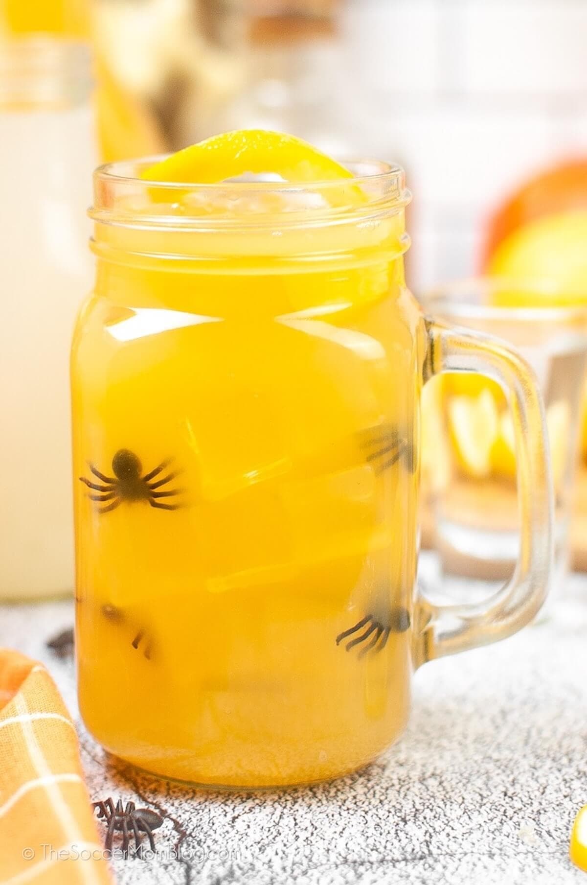 Yellow halloween cocktail in mug decorated with spiders.