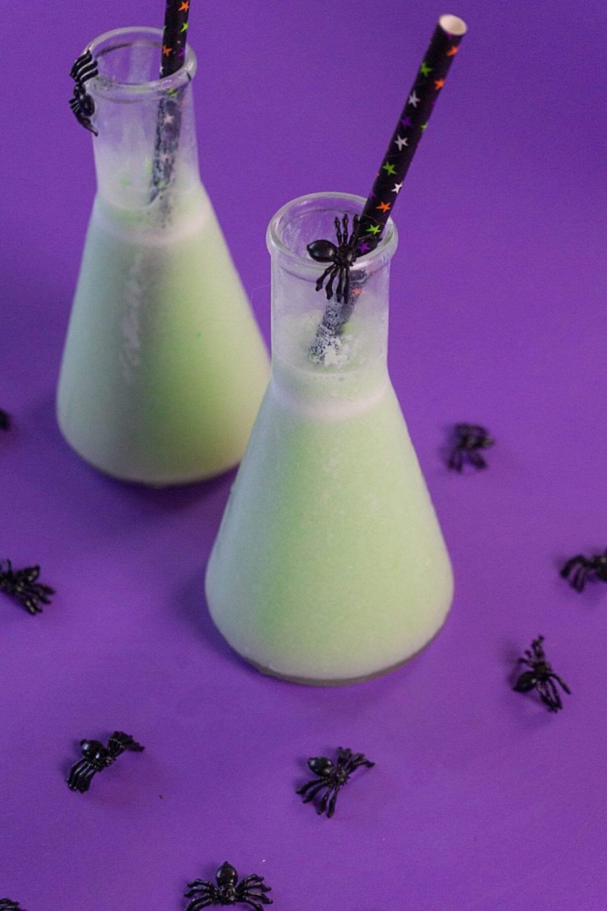 Halloween cocktails in beaker glass surrounded by plastic spiders.