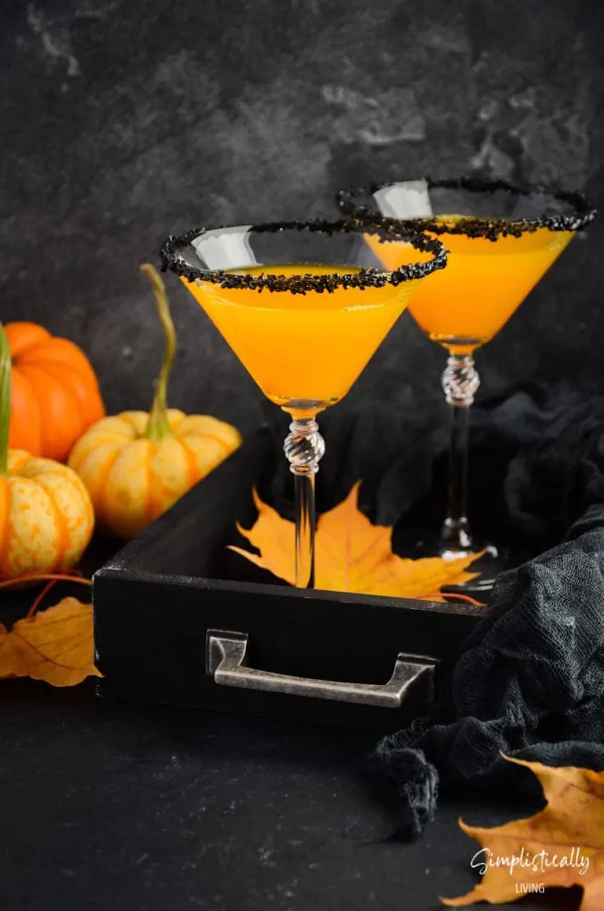 Orange martini in glass ringed with black rimming sugar.