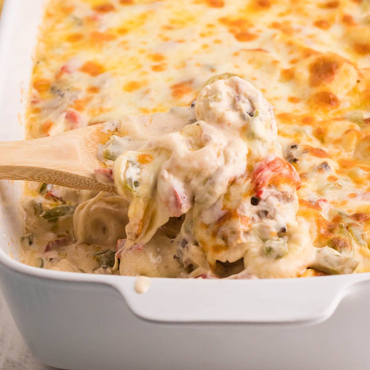 Cheesy baked pasta in casserole dish with spoon.