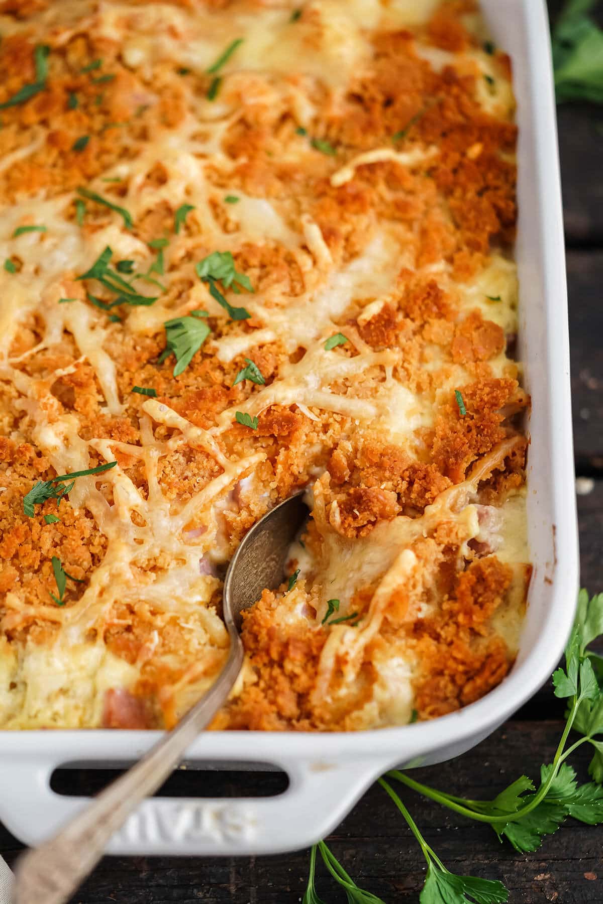 Cheesy chicken casserole with crispy topping in baking dish with serving spoon.