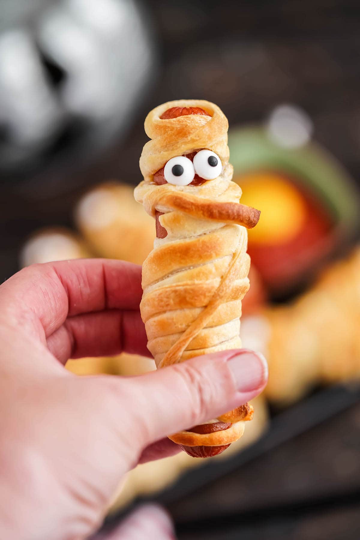 Hand holding baked mummy hot dog.