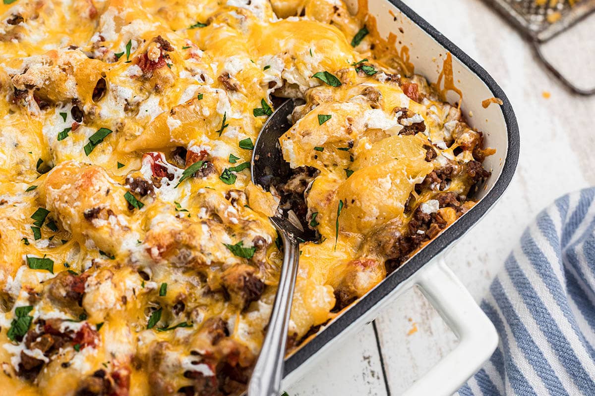 Cheesy pasta casserole in baking dish with serving spoon.