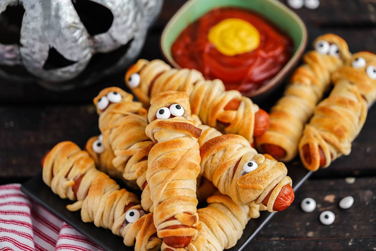 Spooky mummy dogs on platter with halloween decor.