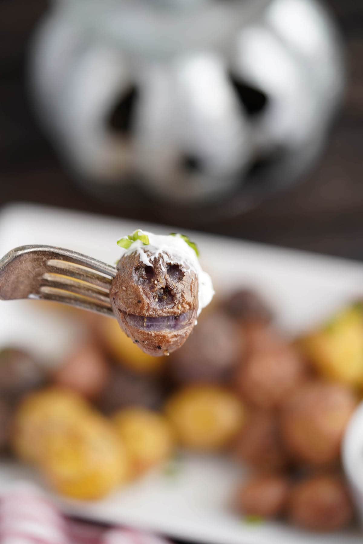 Shrunken Head potato dipped in sour cream on fork.