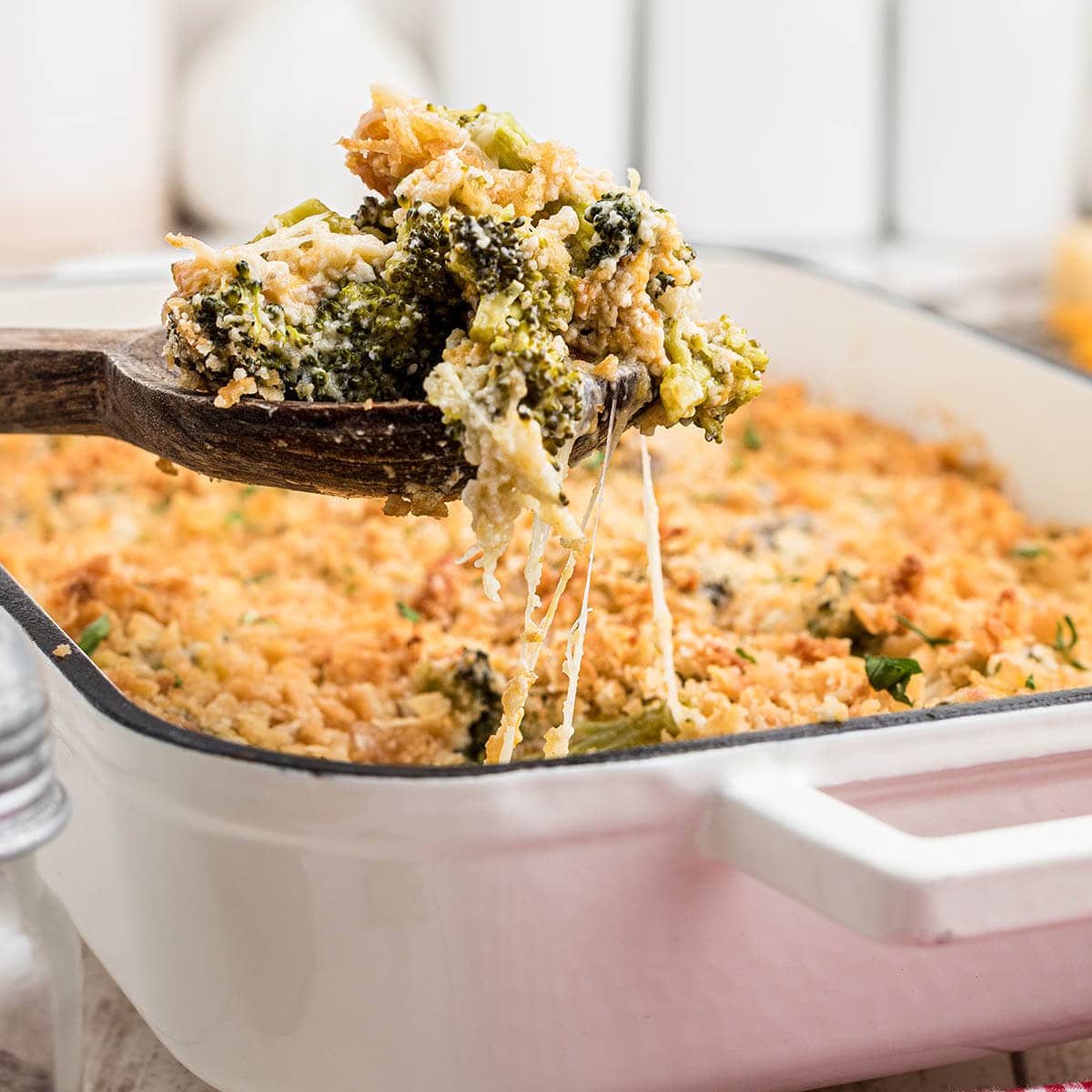Broccoli casserole with crispy topping in baking dish with serving spoon.
