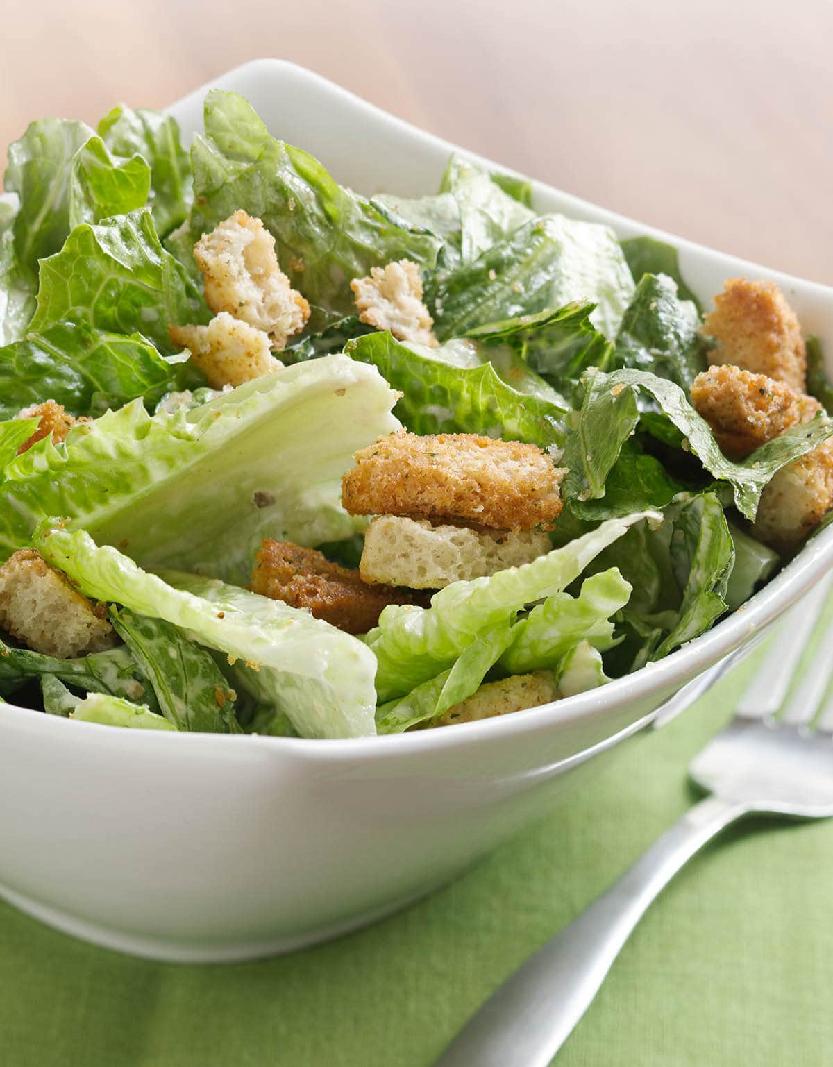 Caesar salad in bowl with serving utensils.