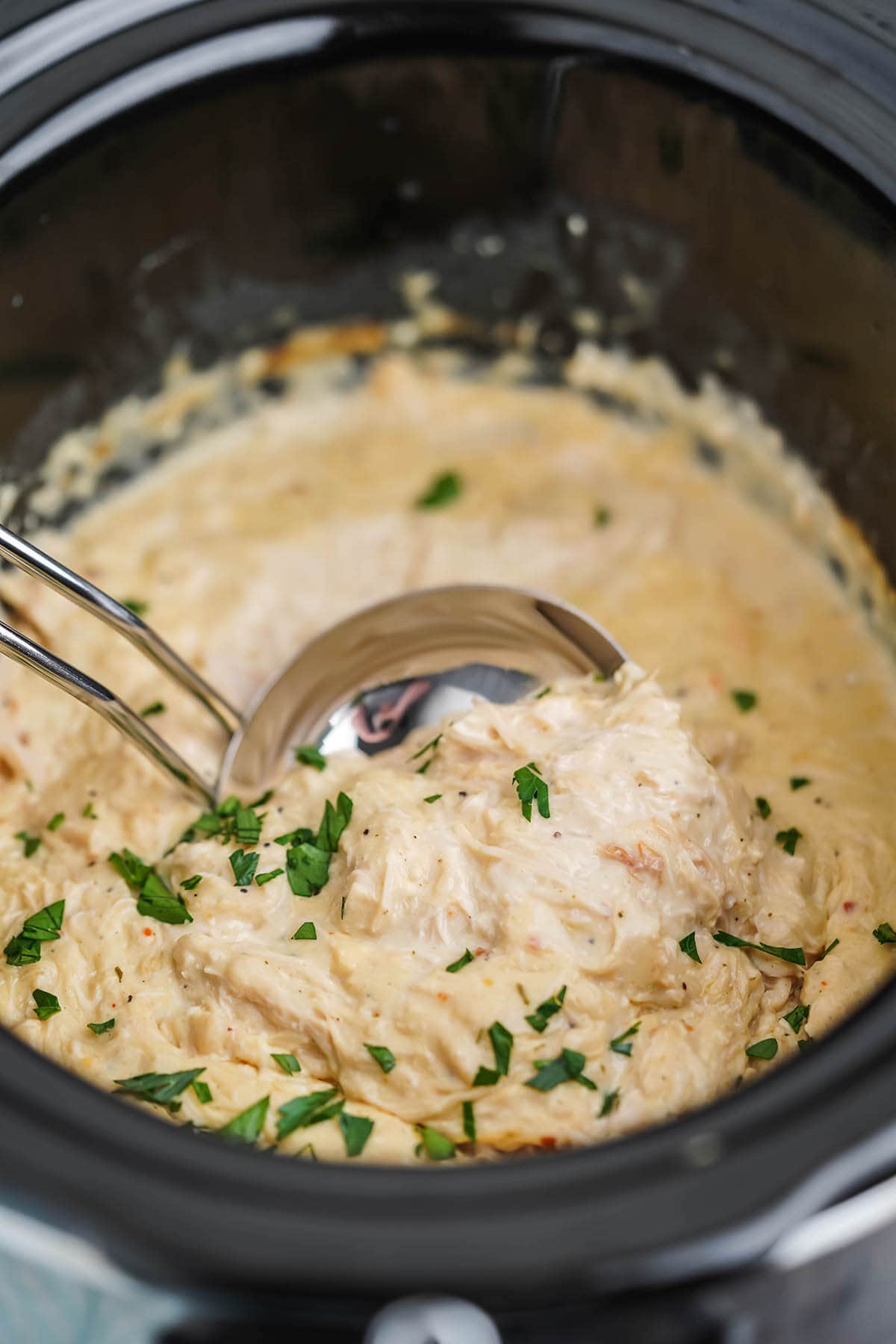 Crockpot filled with Italian shredded chicken with ladle for serving.