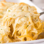 Casserole dish filled with cheesy pasta bake, with serving spoon.