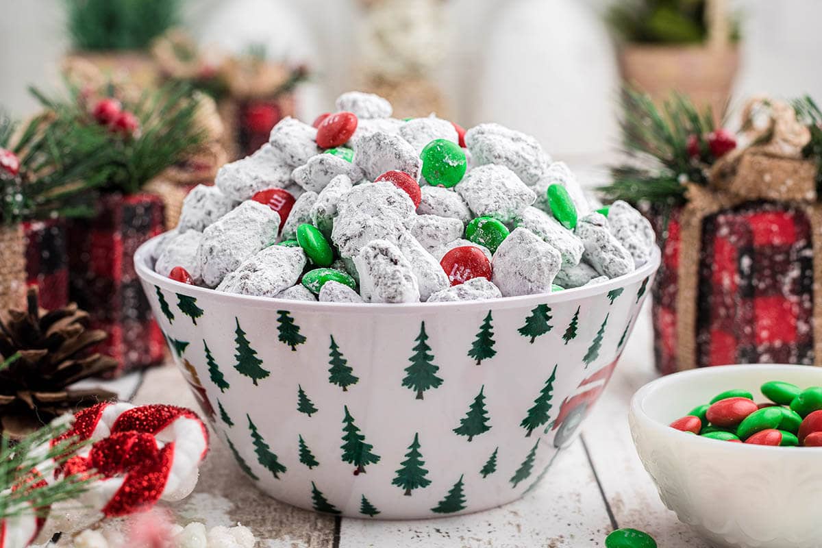 Bowl filled with holiday puppy chow surrounded by Christmas decorations.