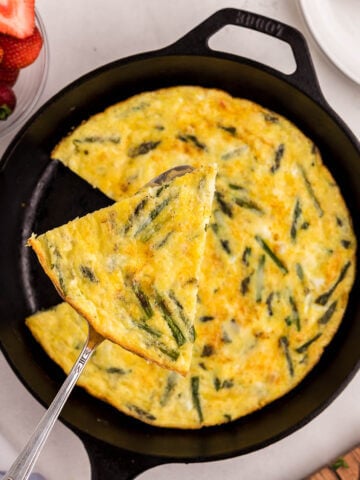 Frittata in cast iron skillet with serving spatula.