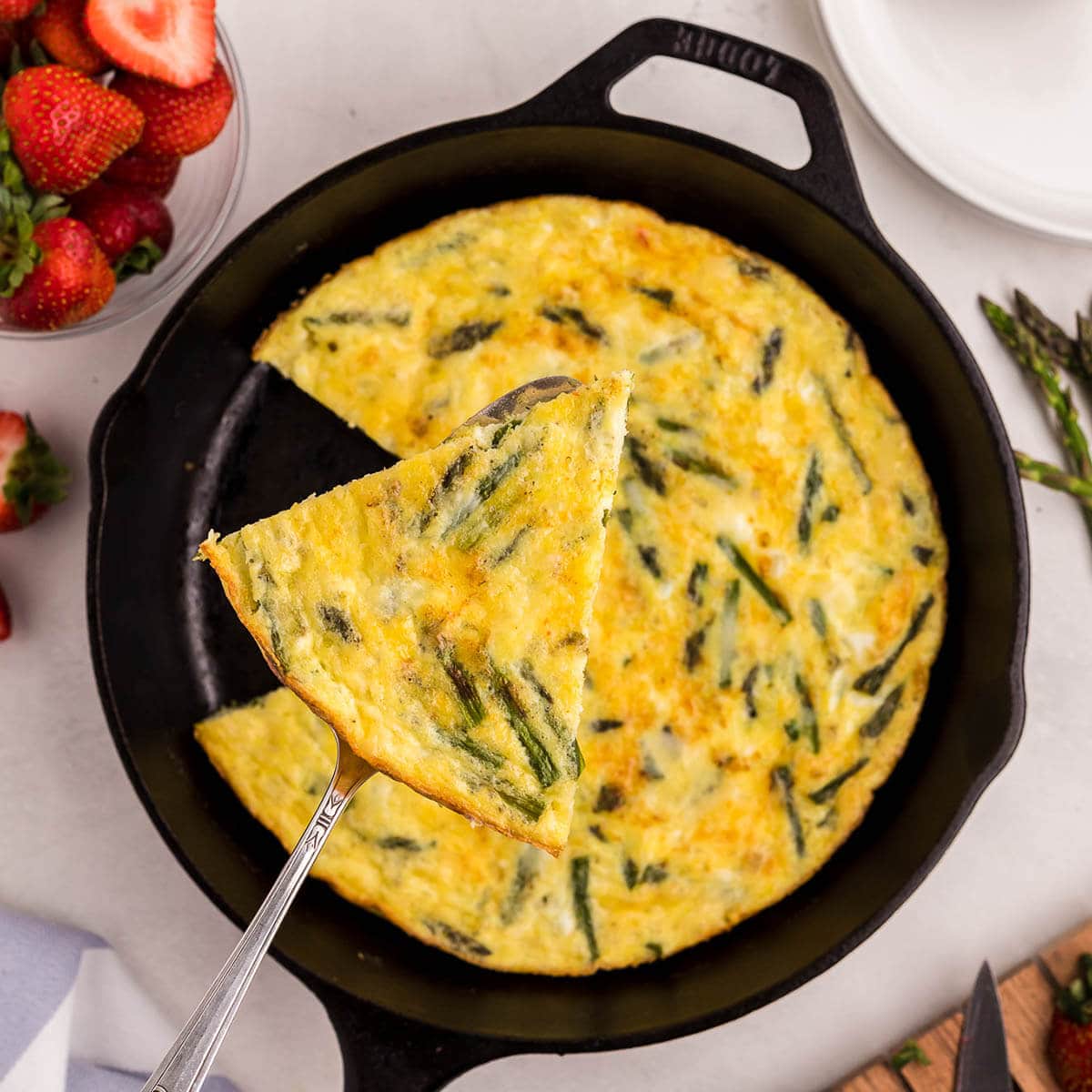 Frittata in cast iron skillet with serving spatula.