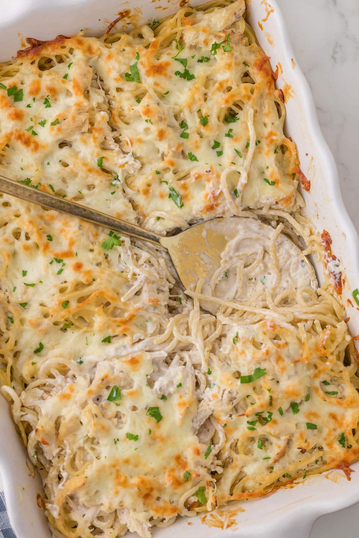 Baking dish filled with spaghetti casserole, with serving spoon.