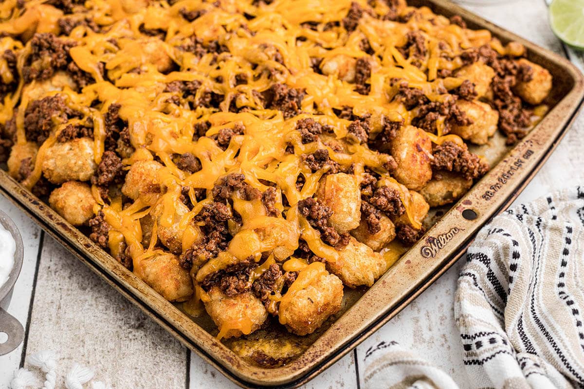 Tater tots nachos on sheet pan topped with taco meat and cheese.
