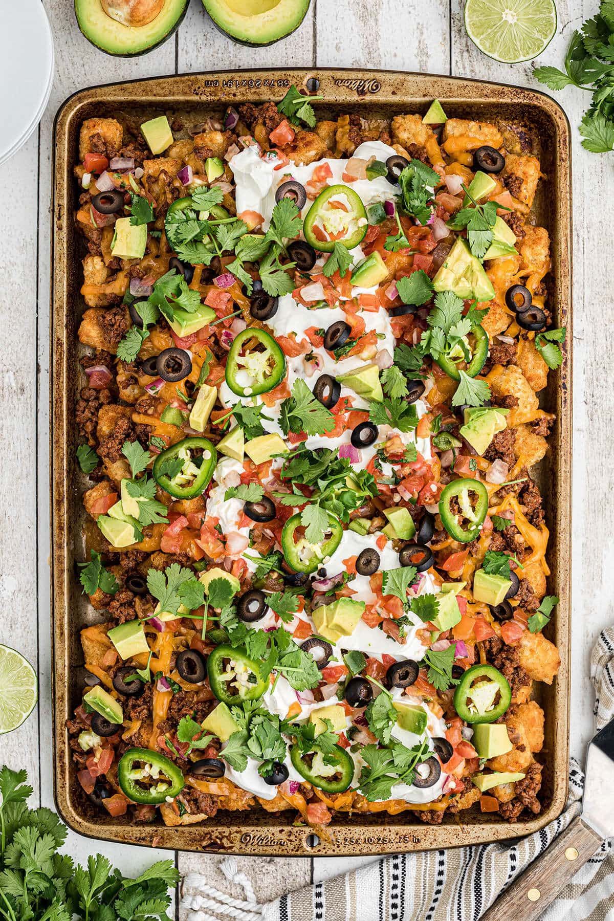 Ground beef tachos on sheet pan topped with olives, sour cream, sliced jalapeños and cheese.