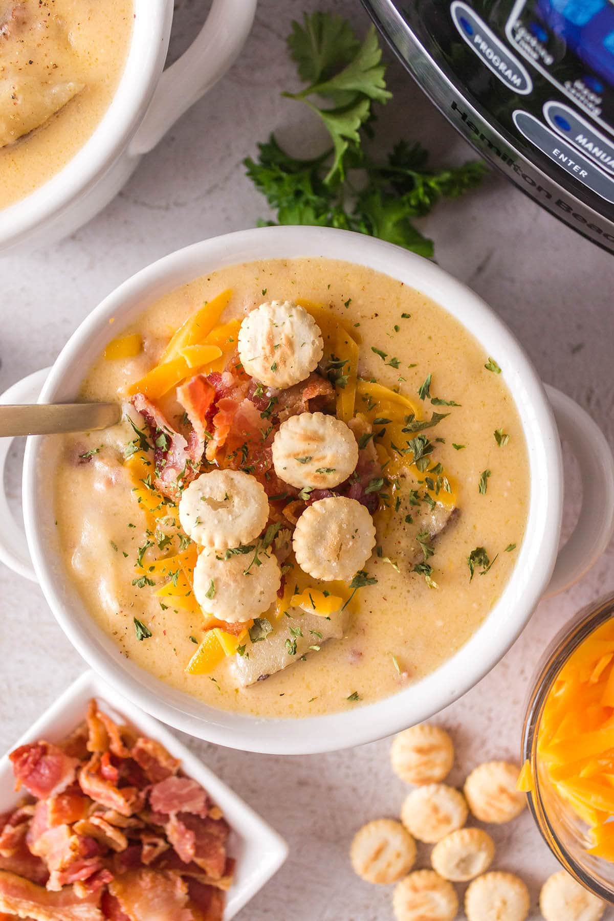 bowl of Crock Pot Potato Soup surrounded by bacon, shredded cheese and crackers.