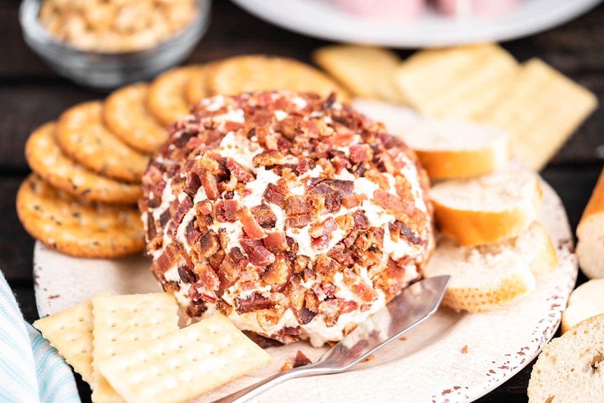 Cheese ball on plate with crackers and serving knife.