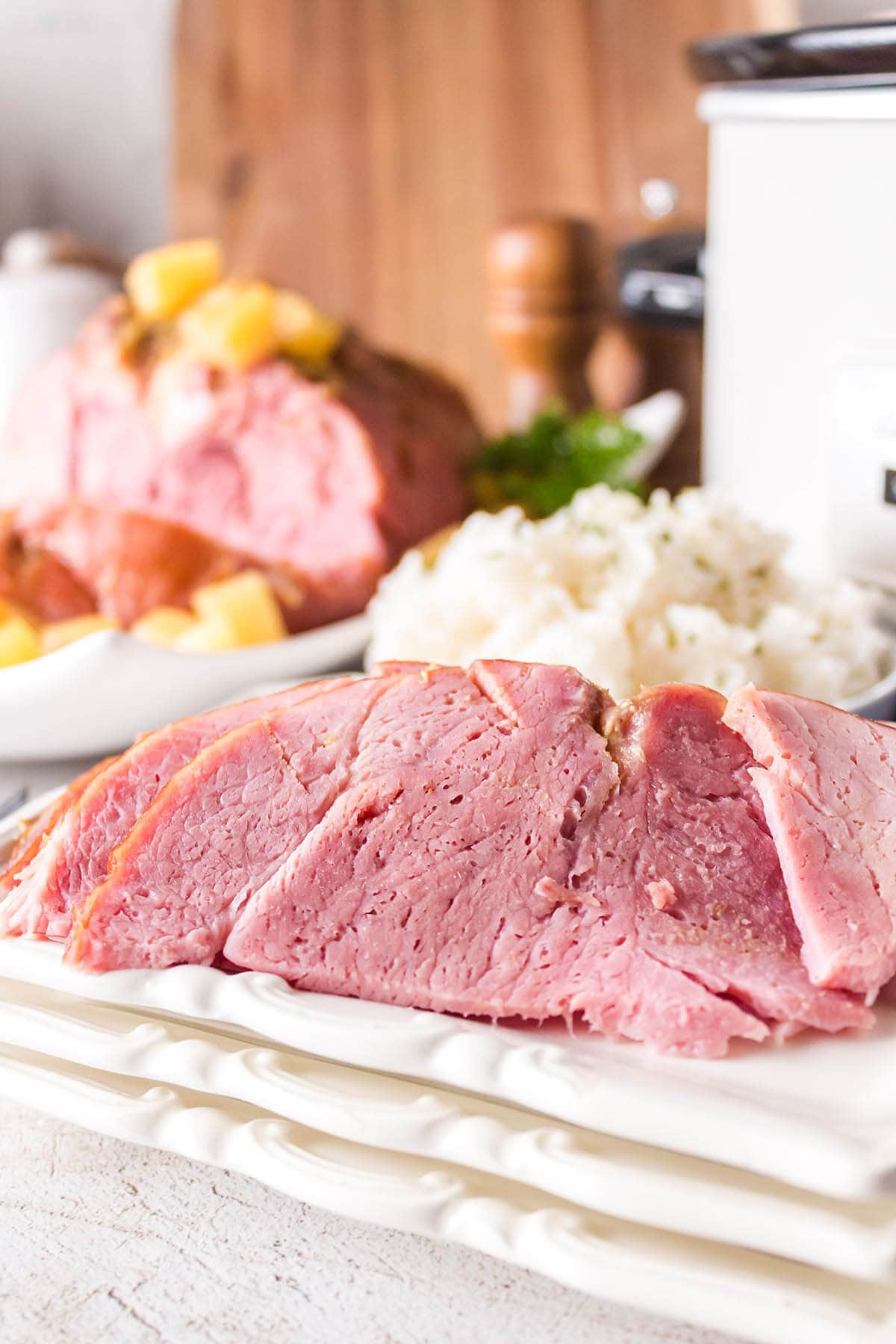 Sliced ham on platter with crockpot in the background.