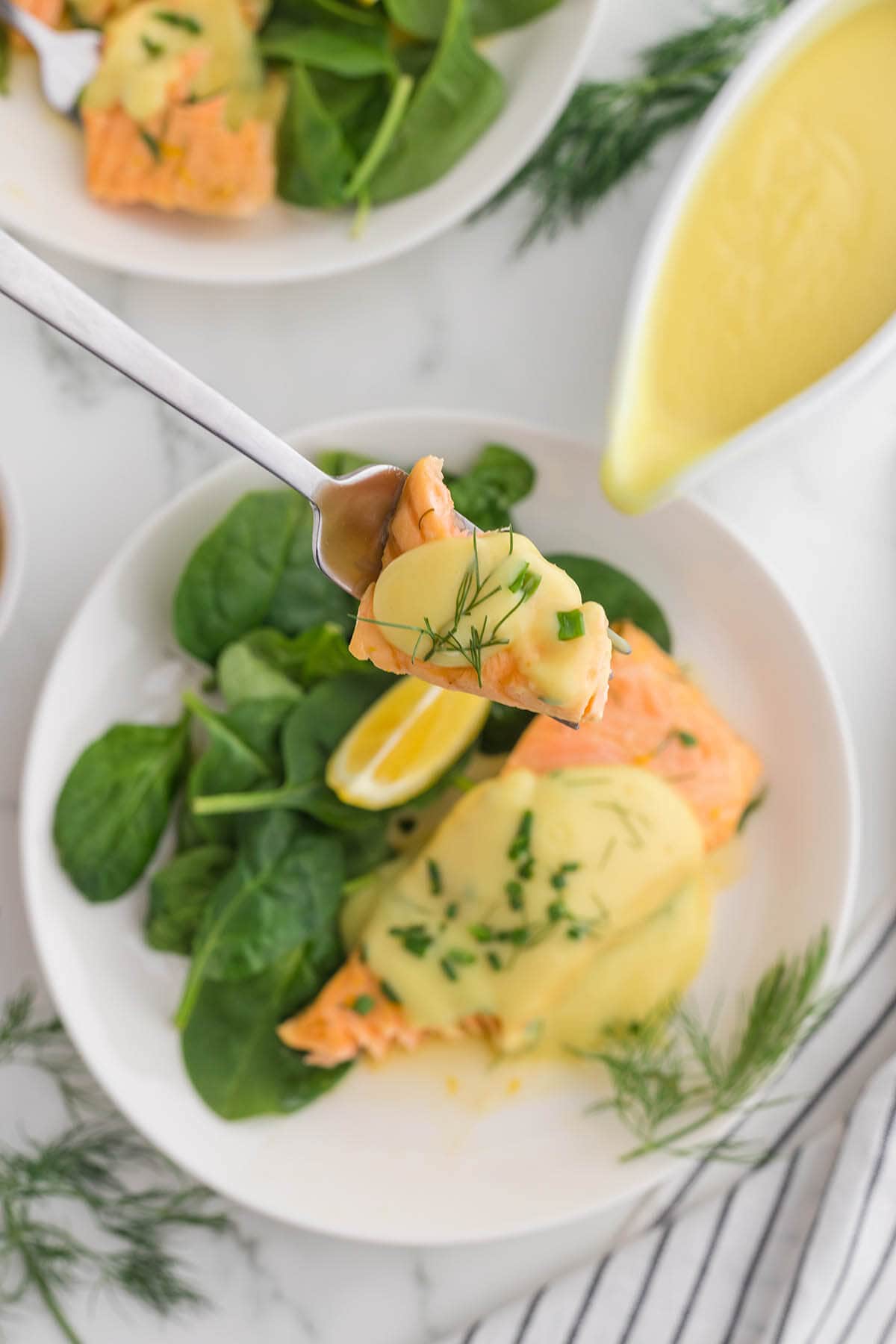 Fork holding poached salmon with hollandaise sauce.