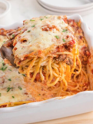 Cheesy Million Dollar Baked Spaghetti in casserole dish with serving spoon.