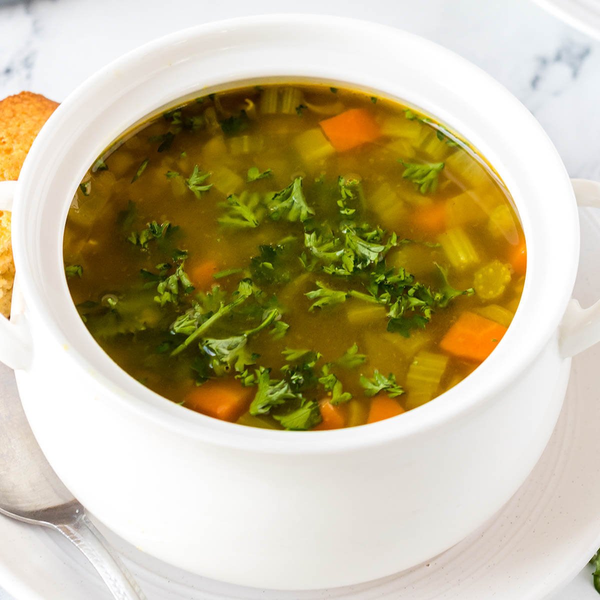 Vegetable soup in bowl with spoon on table.