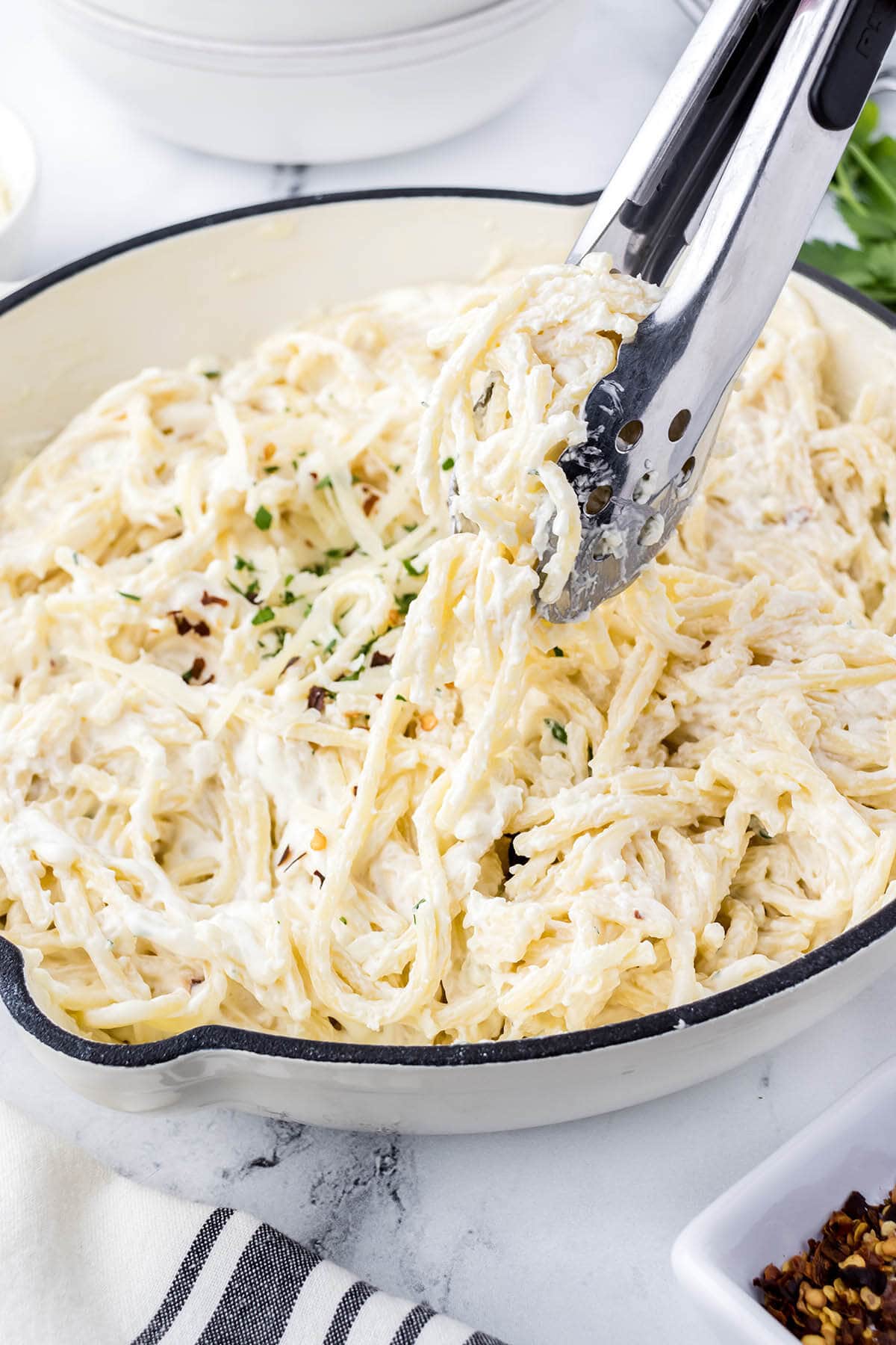 Cream cheese pasta in a serving dish with tongs.