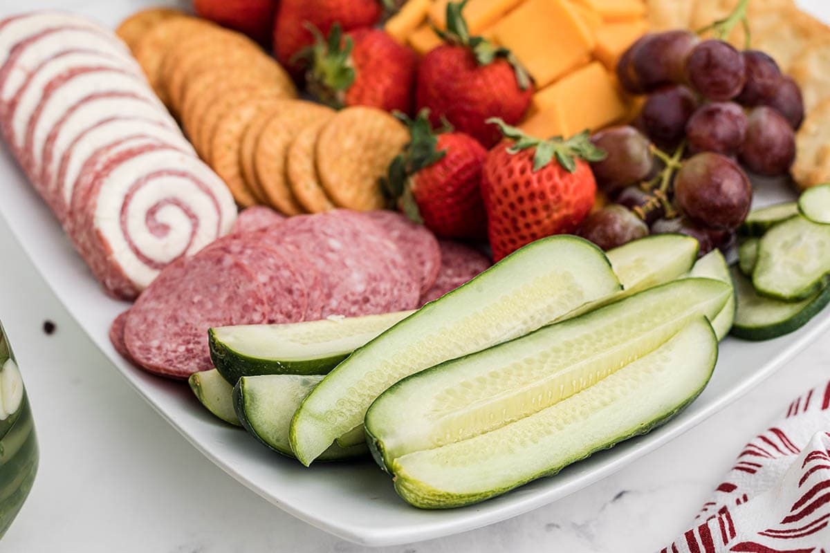 Charcuterie board with cheeses, salami, crackers, strawberries and pickles.