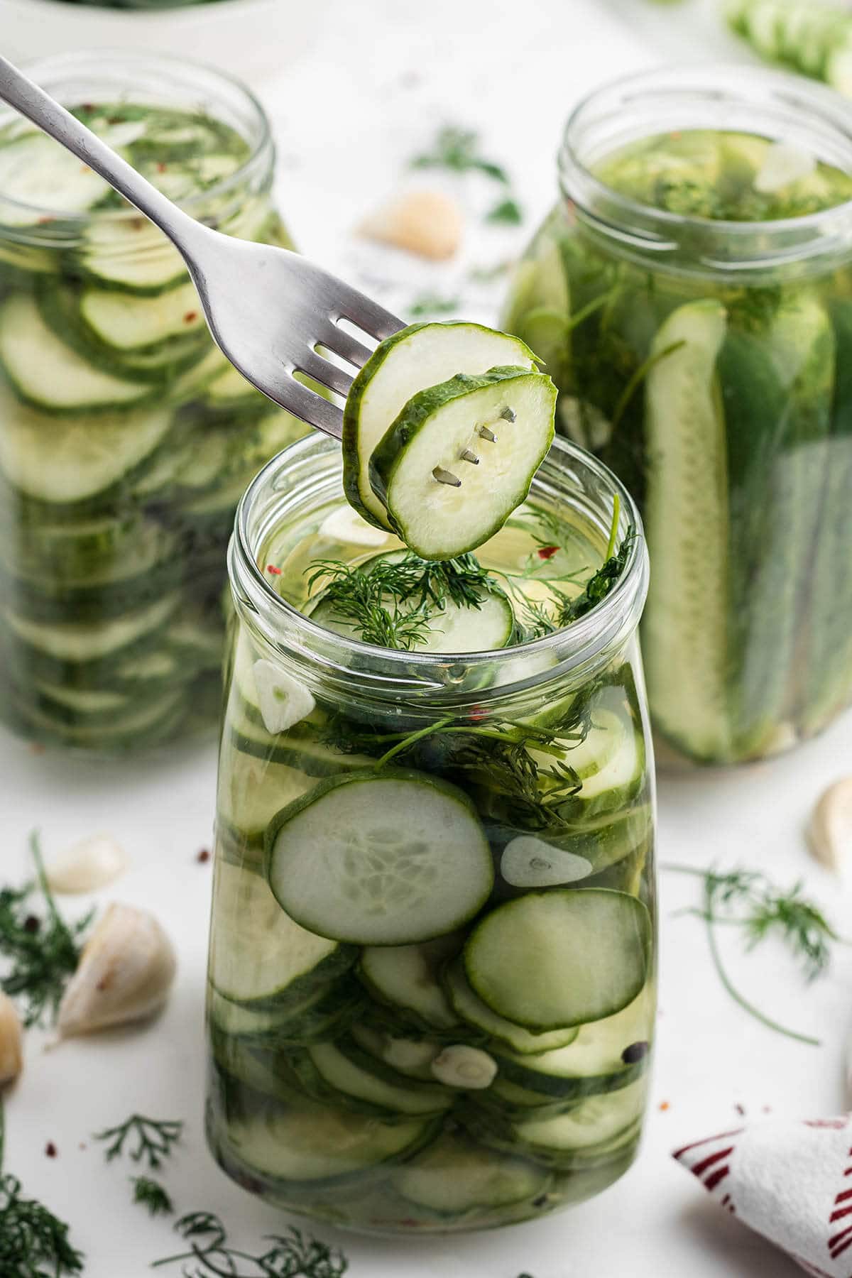 Jars of refrigerator dill pickles with fork stabbing two sliced pickles.