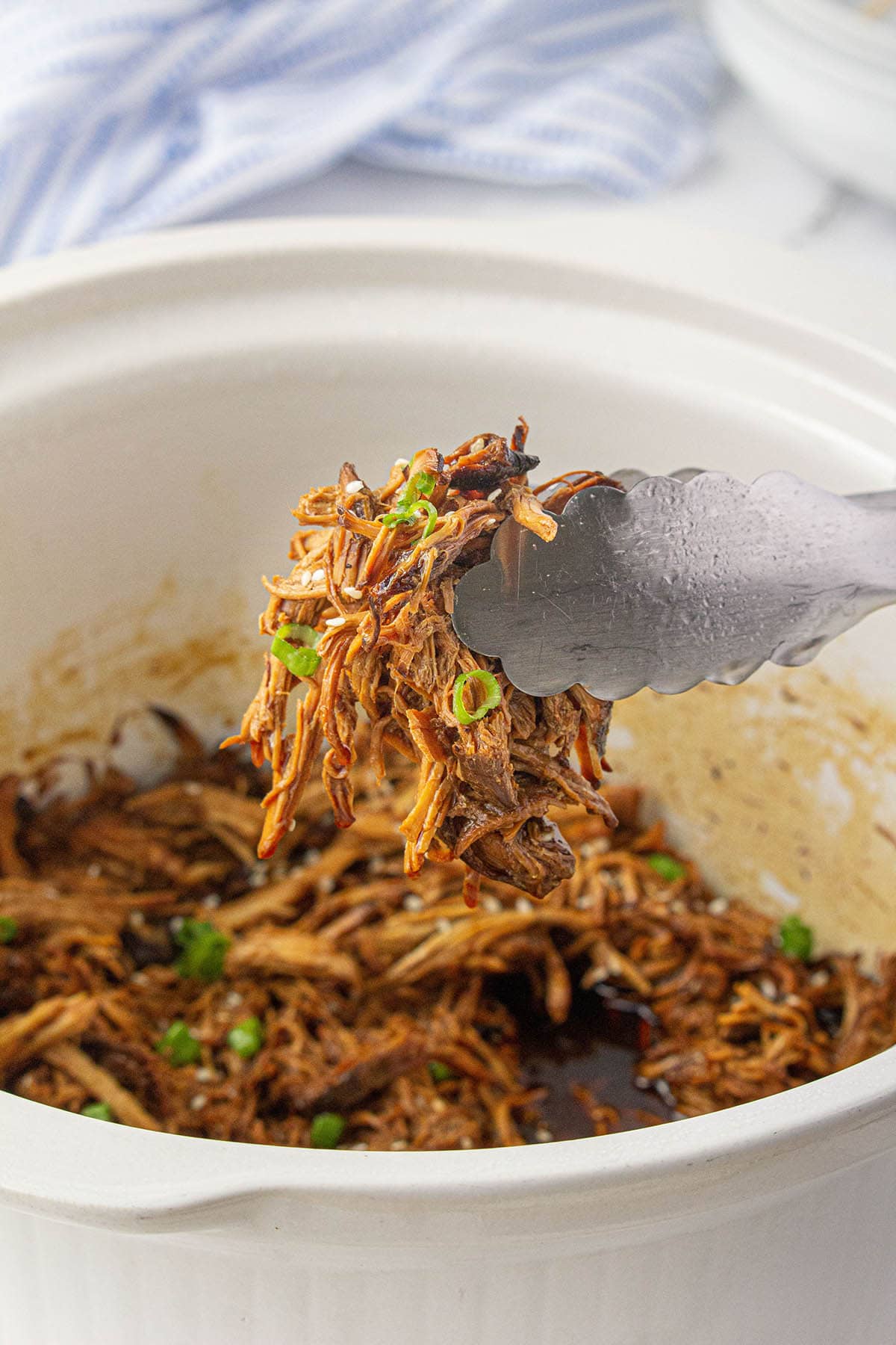 Shredded crock pot teriyaki chicken in slow cooker with serving tongs.