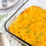 Cheesy zucchini cornbread casserole in baking dish with serving spoon.