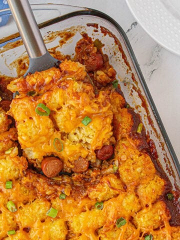 Chili Dog Tater Tot Casserole in a baking dish with a serving spoon.