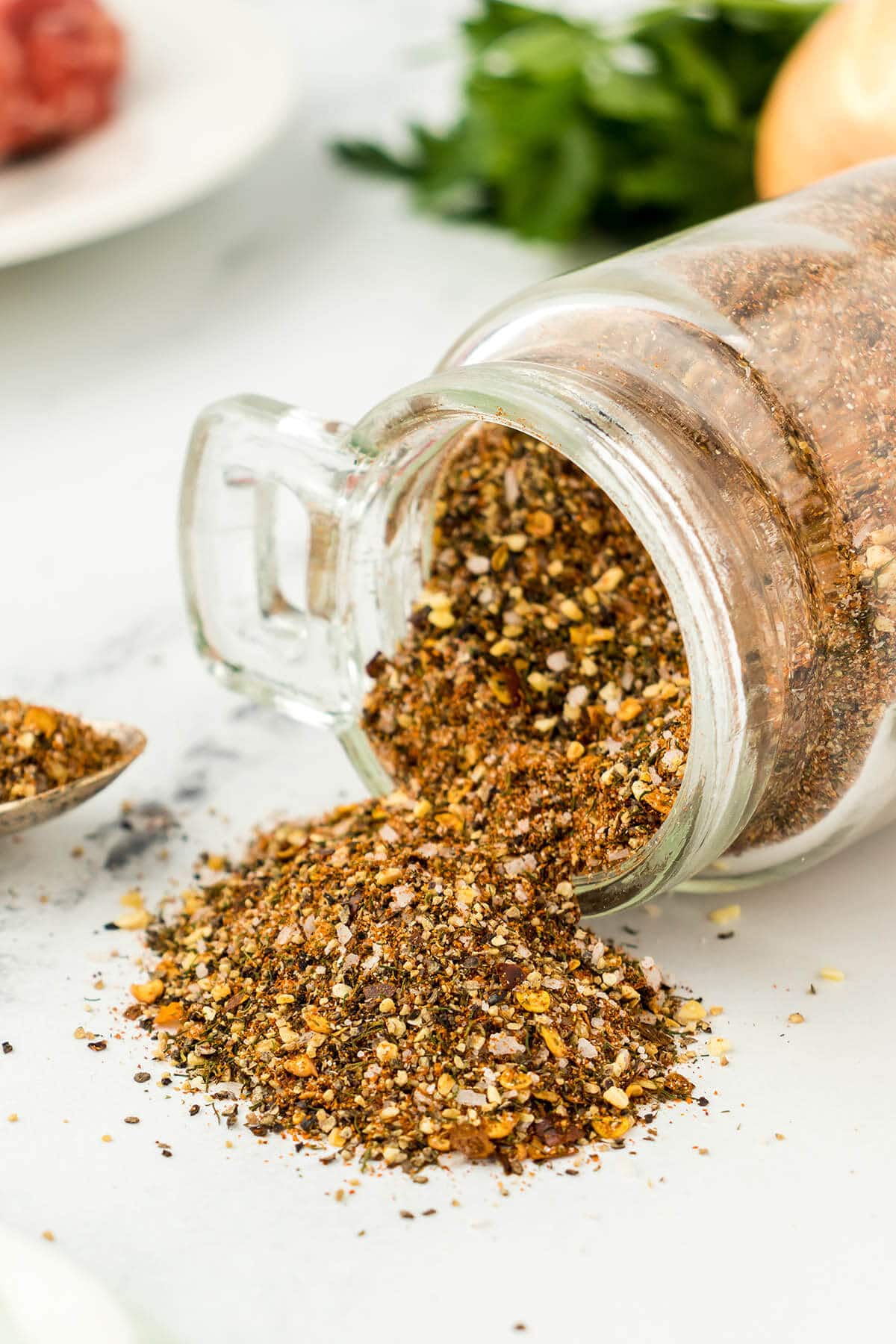 Jar of homemade Montreal steak seasoning on its side, spilling out the spice mix.